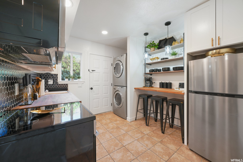 Kitchen with pendant lighting, stainless steel refrigerator, white cabinets, tasteful backsplash, and stacked washer / dryer