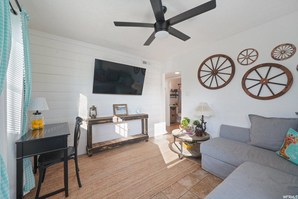 Tiled living room featuring ceiling fan and wooden walls