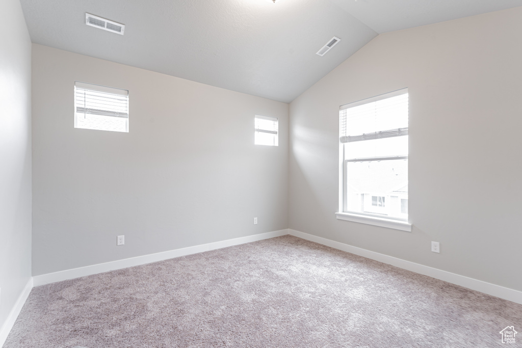Carpeted empty room with plenty of natural light and vaulted ceiling