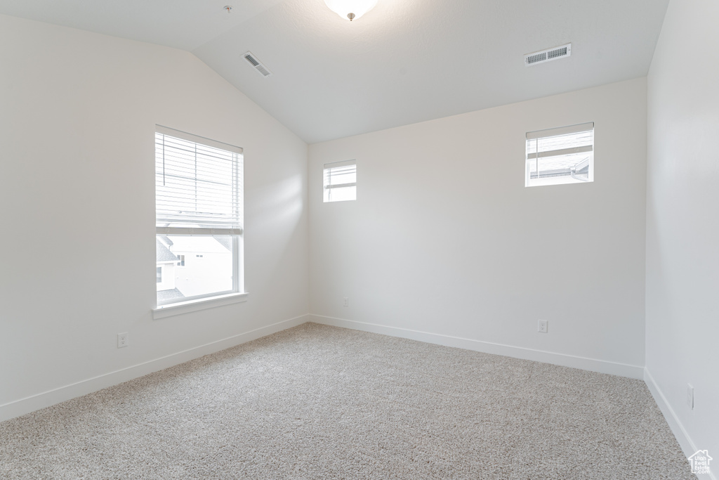 Carpeted empty room featuring lofted ceiling and plenty of natural light