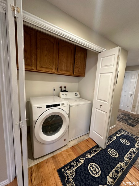 Clothes washing area featuring light hardwood / wood-style flooring, independent washer and dryer, and cabinets