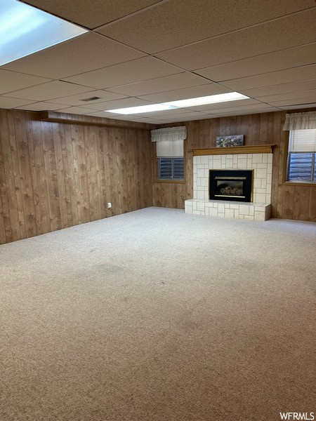 Basement featuring wood walls, a fireplace, a drop ceiling, and carpet flooring