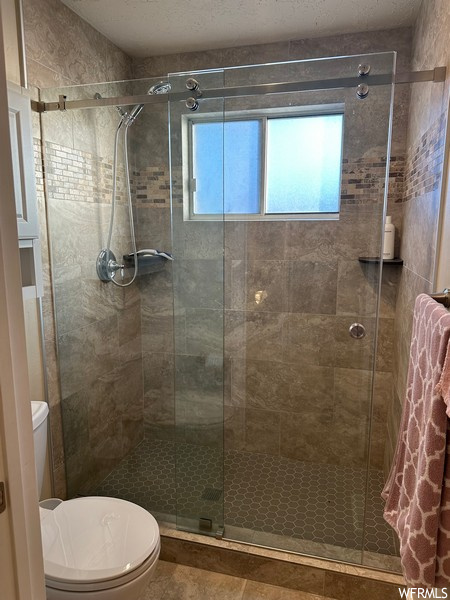 Bathroom featuring toilet, tile flooring, and a shower with shower door