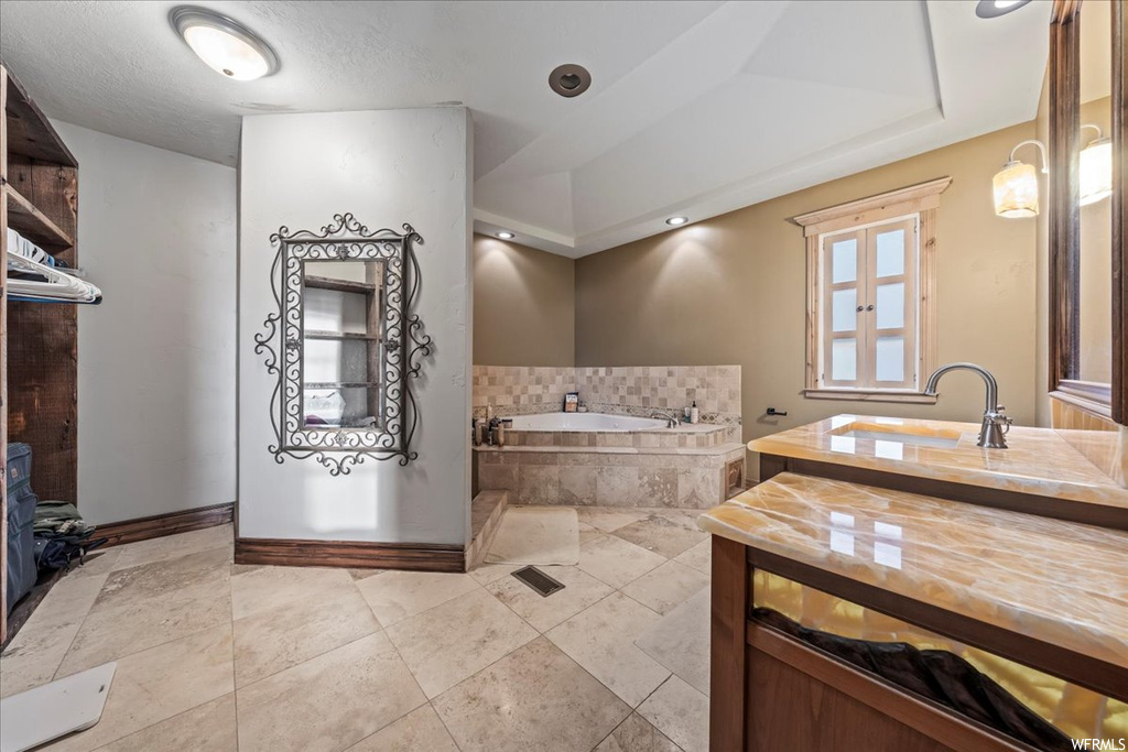 Bathroom with tile flooring, a tray ceiling, tiled tub, and large vanity