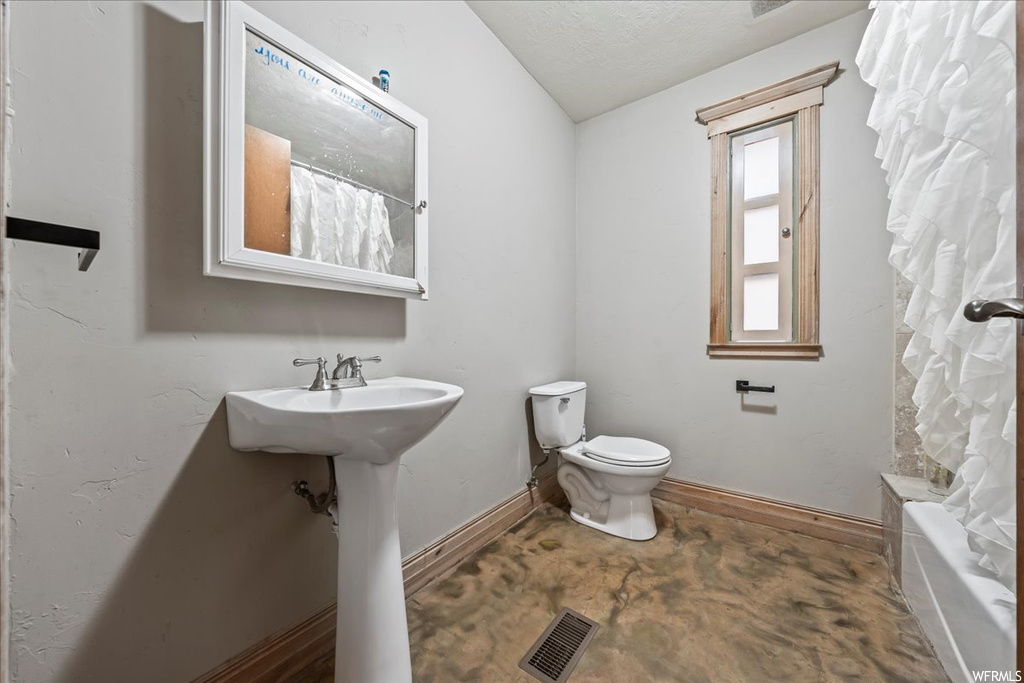 Full bathroom with sink, shower / bath combo, concrete floors, toilet, and a textured ceiling