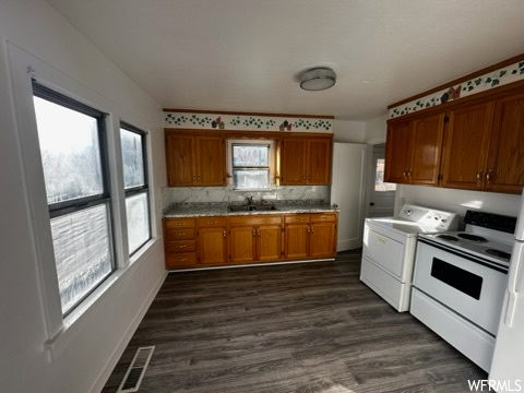 Kitchen featuring white electric range oven, sink, dark hardwood / wood-style flooring, backsplash, and independent washer and dryer