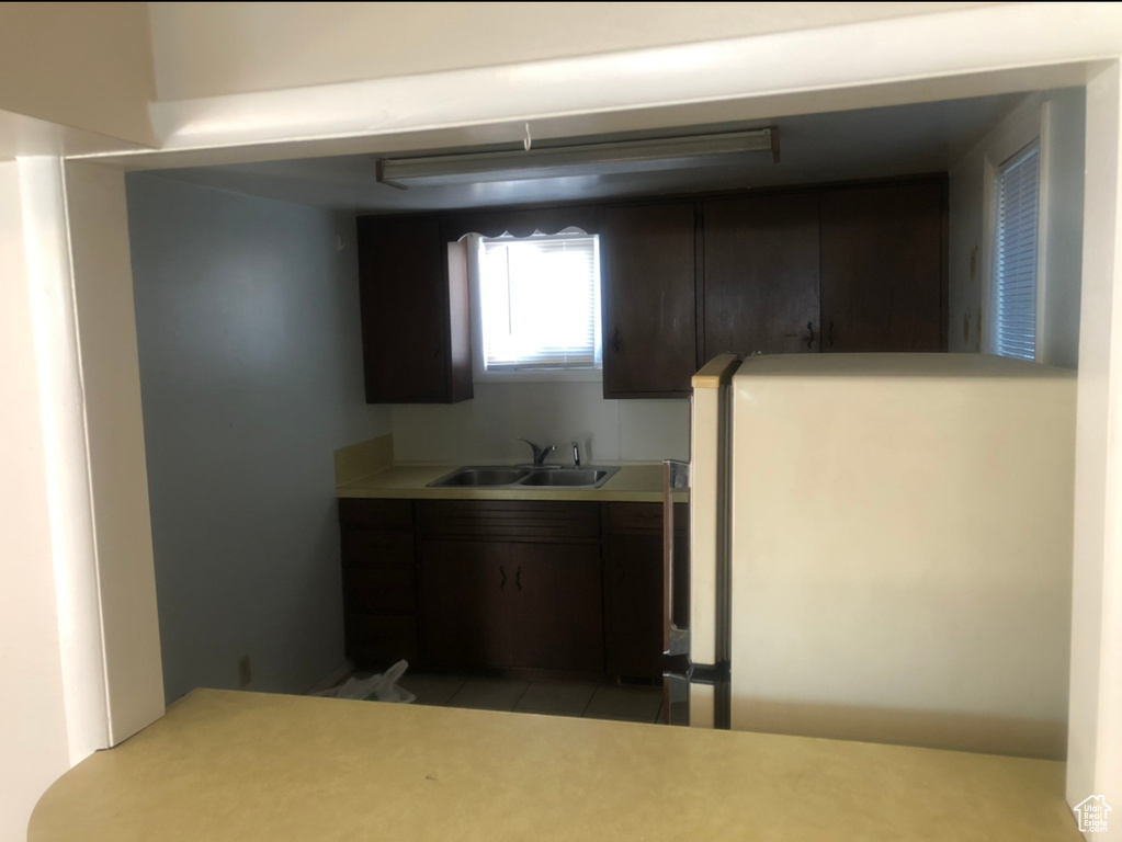 Kitchen featuring sink, light tile flooring, dark brown cabinets, and refrigerator