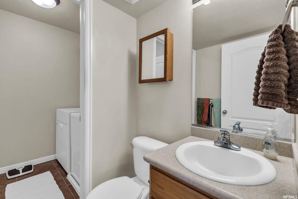 Bathroom featuring toilet, tile flooring, washing machine and dryer, and vanity with extensive cabinet space