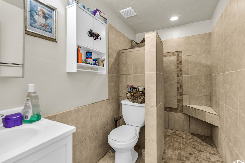 Bathroom featuring toilet, tile walls, a tile shower, tile flooring, and vanity