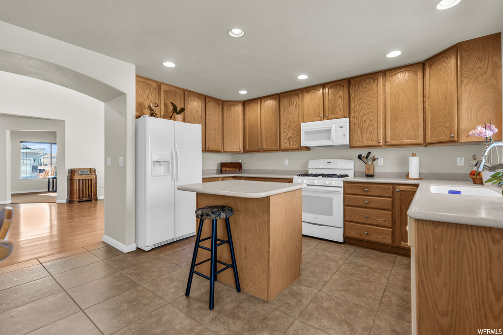 Kitchen with light tile flooring, sink, a center island, white appliances, and a breakfast bar