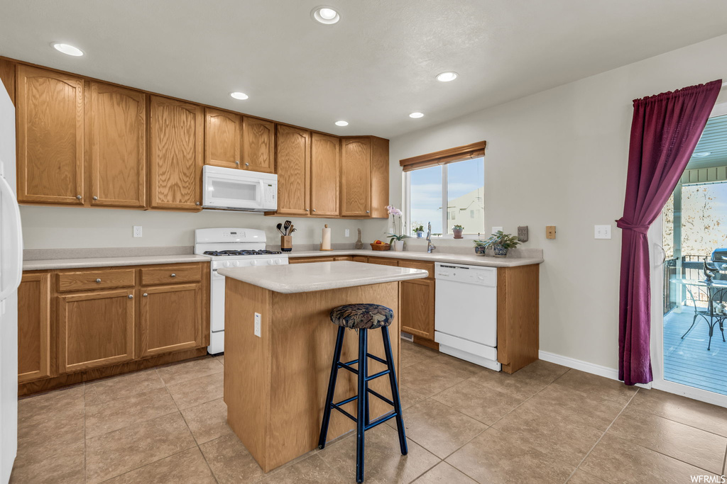 Kitchen with white appliances, a breakfast bar, a center island, and light tile floors