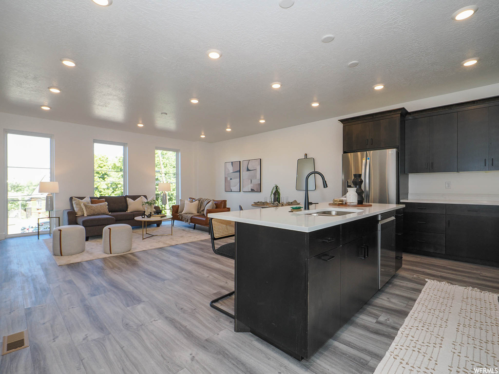 Kitchen featuring sink, light hardwood / wood-style flooring, a kitchen island with sink, appliances with stainless steel finishes, and a breakfast bar