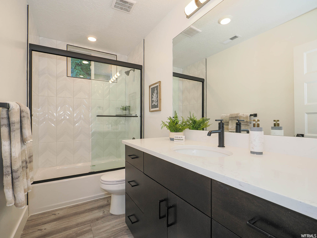 Full bathroom with vanity, toilet, a textured ceiling, combined bath / shower with glass door, and wood-type flooring