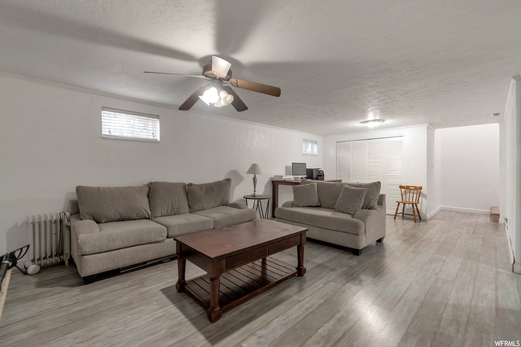 Living room featuring a textured ceiling, ceiling fan, light wood-type flooring, and radiator heating unit