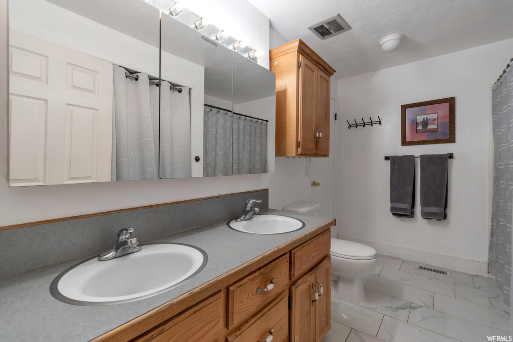 Bathroom featuring dual sinks, toilet, tile floors, and vanity with extensive cabinet space