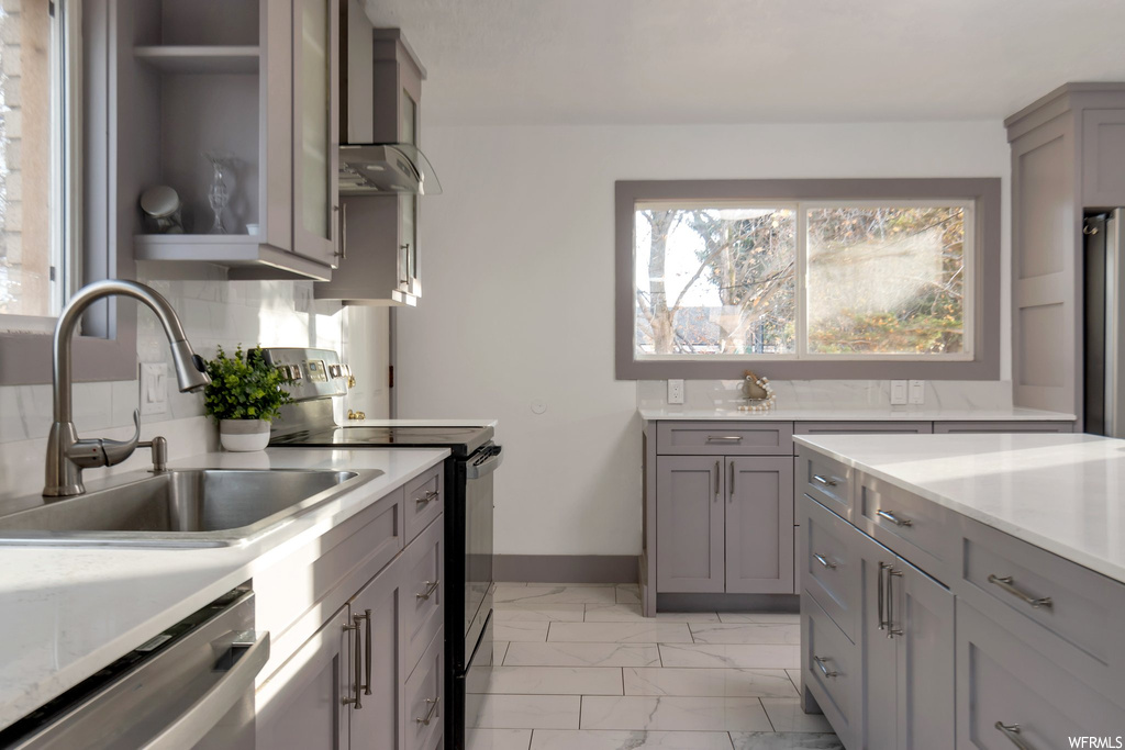 Kitchen featuring gray cabinetry, wall chimney range hood, tasteful backsplash, stainless steel appliances, and light tile floors