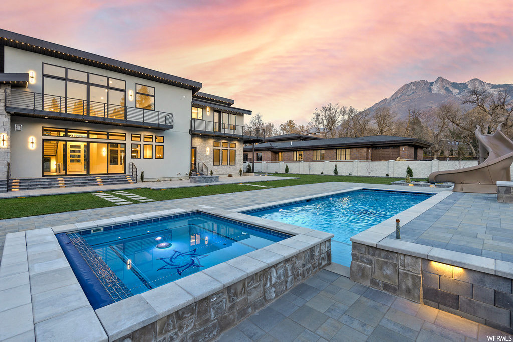 Pool at dusk with a patio area, an in ground hot tub, a water slide, and a mountain view