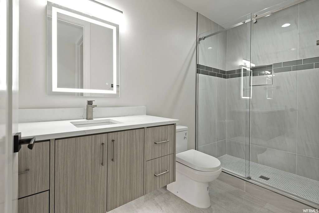 Bathroom featuring toilet, tile floors, a tile shower, and vanity with extensive cabinet space