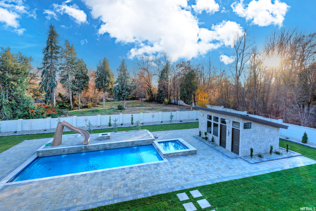 View of swimming pool with a water slide, an outdoor hot tub, a patio area, and a lawn