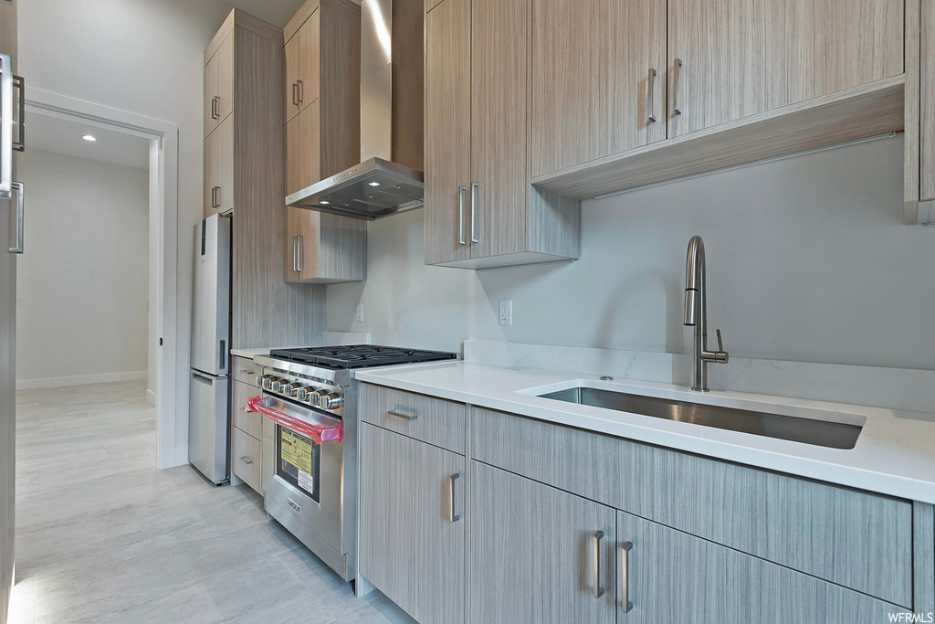 Kitchen with sink, wall chimney range hood, stainless steel fridge, gas range, and light wood-type flooring