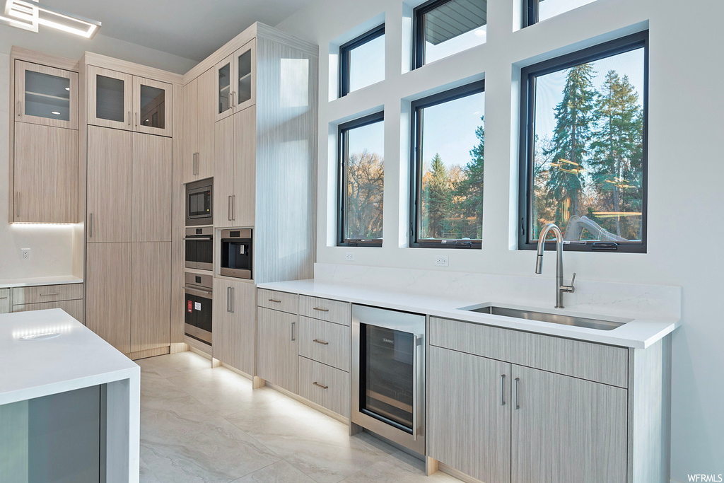 Kitchen featuring sink, light tile flooring, wine cooler, stainless steel microwave, and light brown cabinetry