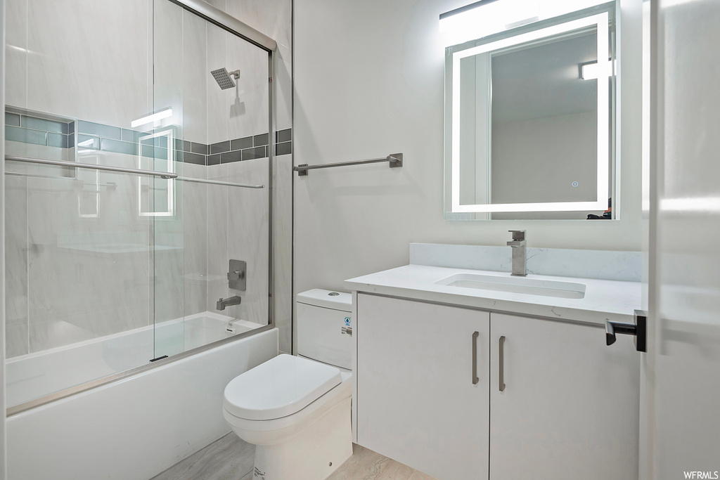 Full bathroom featuring toilet, large vanity, shower / bath combination with glass door, and hardwood / wood-style floors