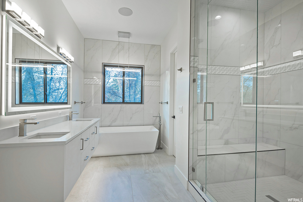 Bathroom with tile flooring, double sink vanity, tile walls, and shower with separate bathtub