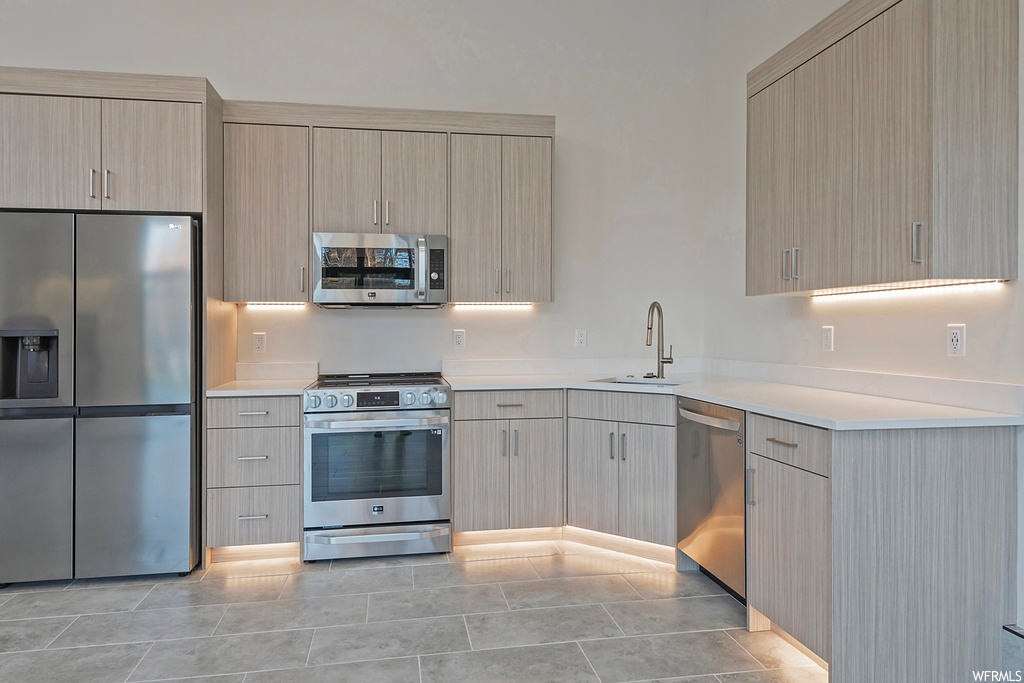 Kitchen featuring light tile floors, light brown cabinetry, sink, and appliances with stainless steel finishes