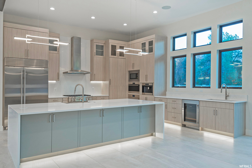 Kitchen with sink, a center island with sink, pendant lighting, beverage cooler, and wall chimney exhaust hood