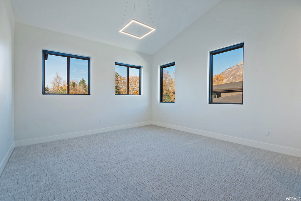 Unfurnished room with light colored carpet, a healthy amount of sunlight, and vaulted ceiling