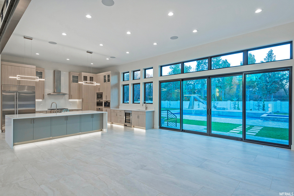 Kitchen featuring sink, a kitchen island with sink, built in appliances, pendant lighting, and wall chimney exhaust hood