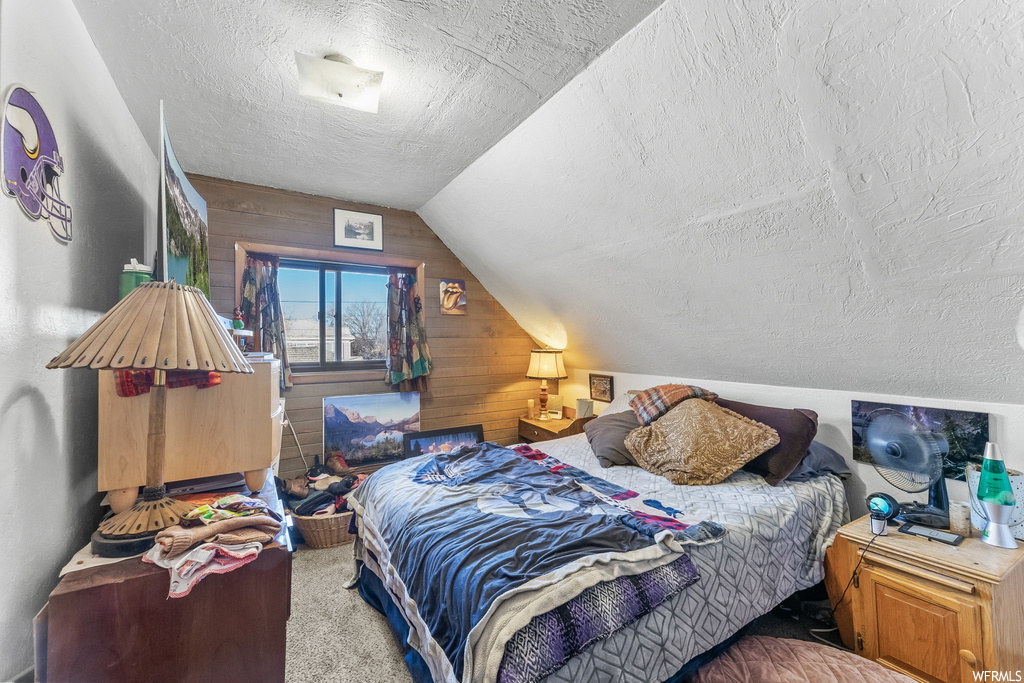 Bedroom with lofted ceiling, light carpet, a textured ceiling, and wood walls