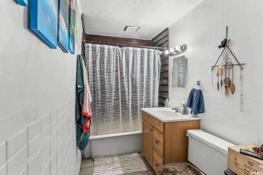 Full bathroom featuring toilet, shower / tub combo with curtain, tile walls, and vanity