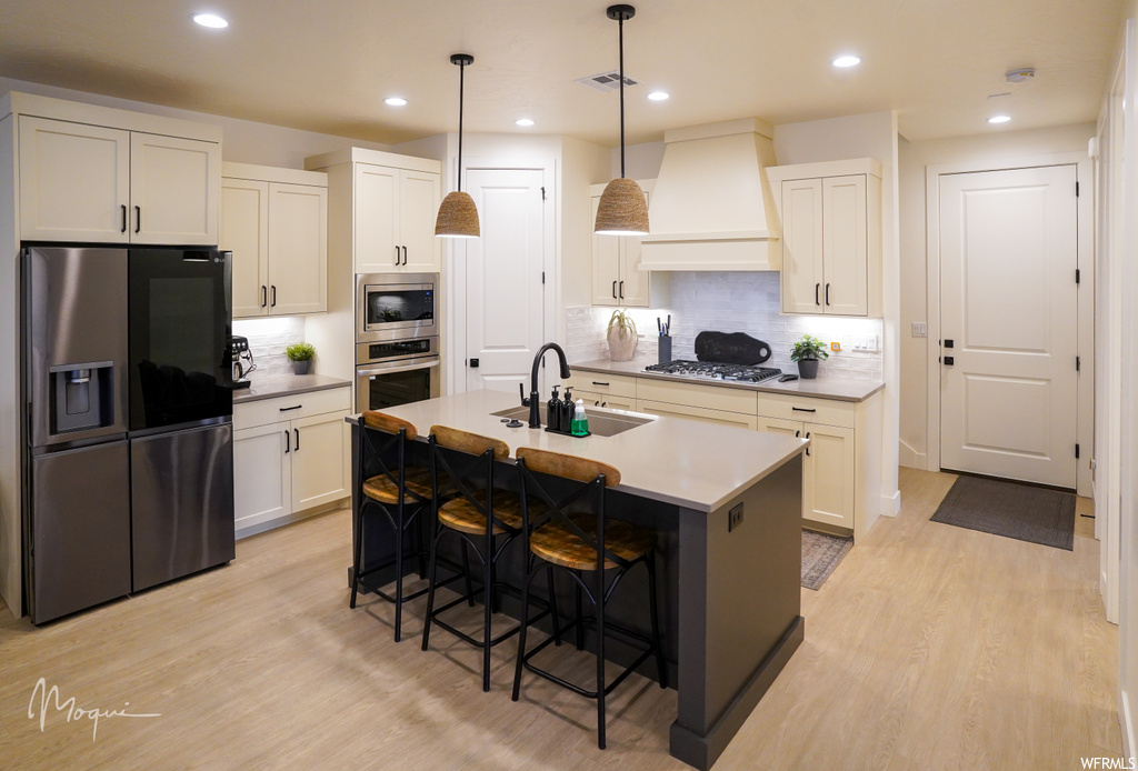 Kitchen with premium range hood, sink, appliances with stainless steel finishes, a kitchen island with sink, and tasteful backsplash