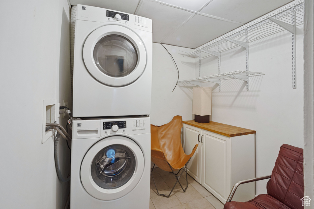 Clothes washing area with light tile flooring, stacked washer / dryer, hookup for a washing machine, and cabinets