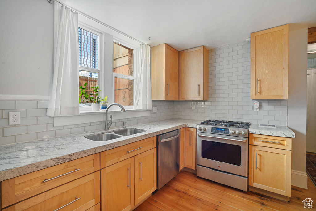 Kitchen with sink, tasteful backsplash, light wood-type flooring, stainless steel appliances, and light stone countertops