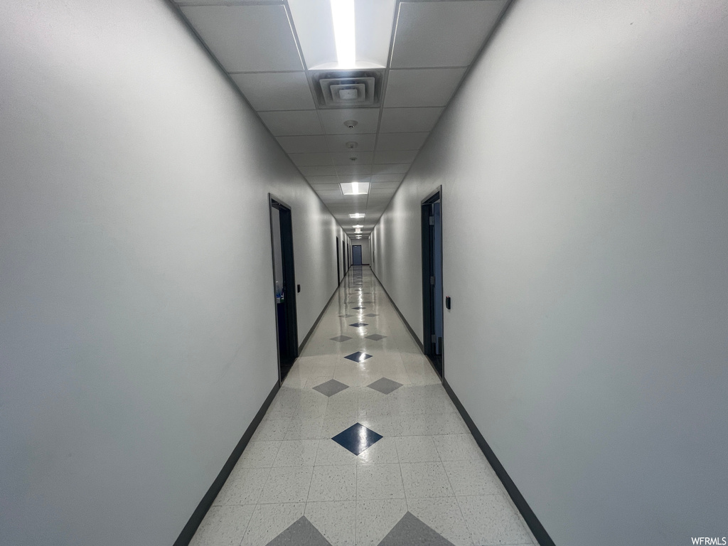 Hallway with light tile flooring and a drop ceiling