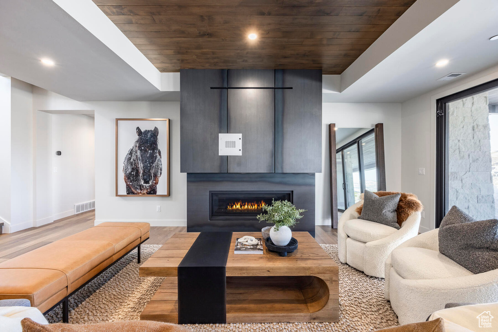 Living room with a large fireplace, light hardwood / wood-style floors, and wood ceiling