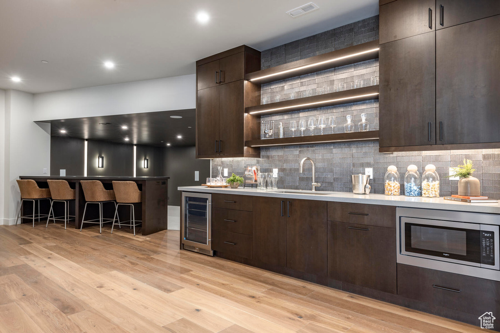 Kitchen with tasteful backsplash, light wood-type flooring, stainless steel microwave, and wine cooler