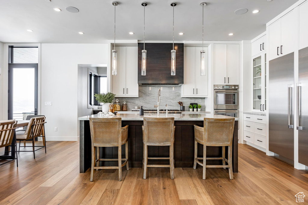 Kitchen with hanging light fixtures, light wood-type flooring, a kitchen island with sink, and a kitchen breakfast bar