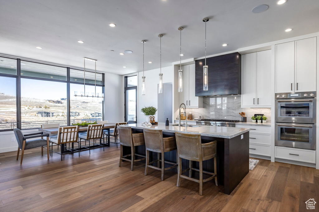 Kitchen featuring light stone counters, dark hardwood / wood-style floors, pendant lighting, tasteful backsplash, and appliances with stainless steel finishes