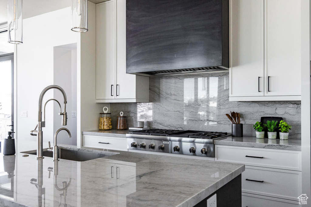 Kitchen with tasteful backsplash, light stone countertops, custom range hood, hanging light fixtures, and white cabinetry