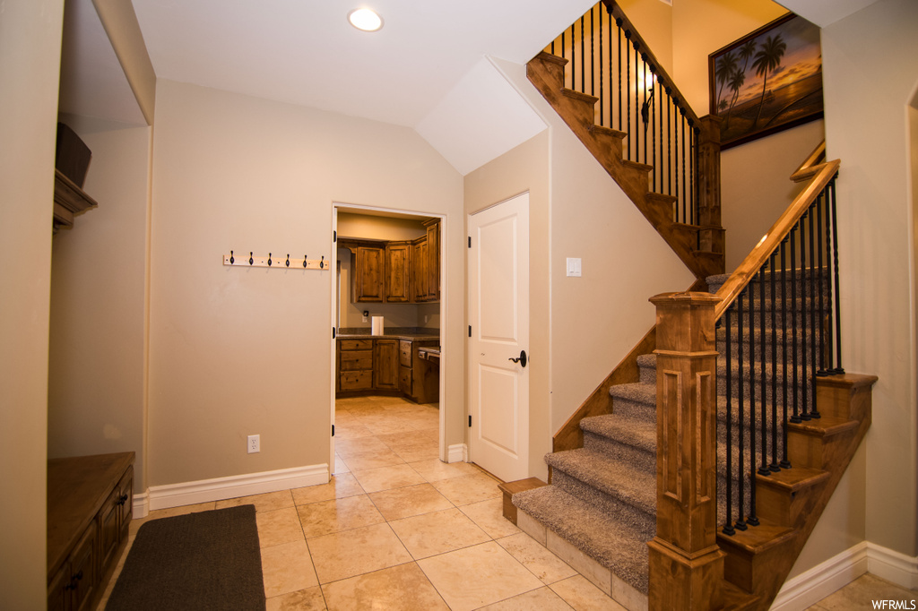 Stairway featuring light tile floors and vaulted ceiling