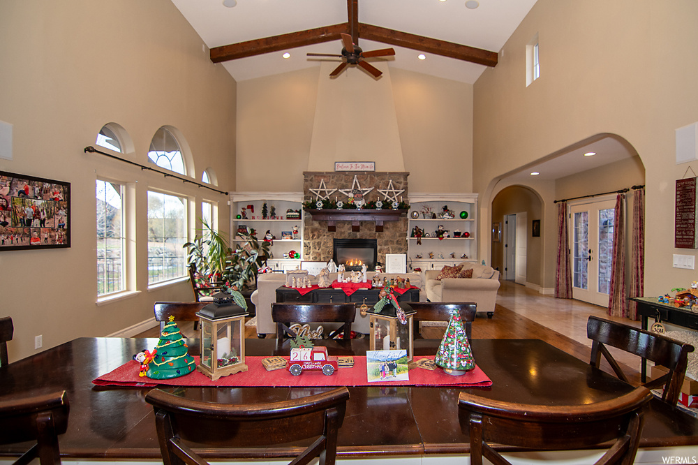 Tiled dining space with high vaulted ceiling, ceiling fan, a fireplace, and beamed ceiling