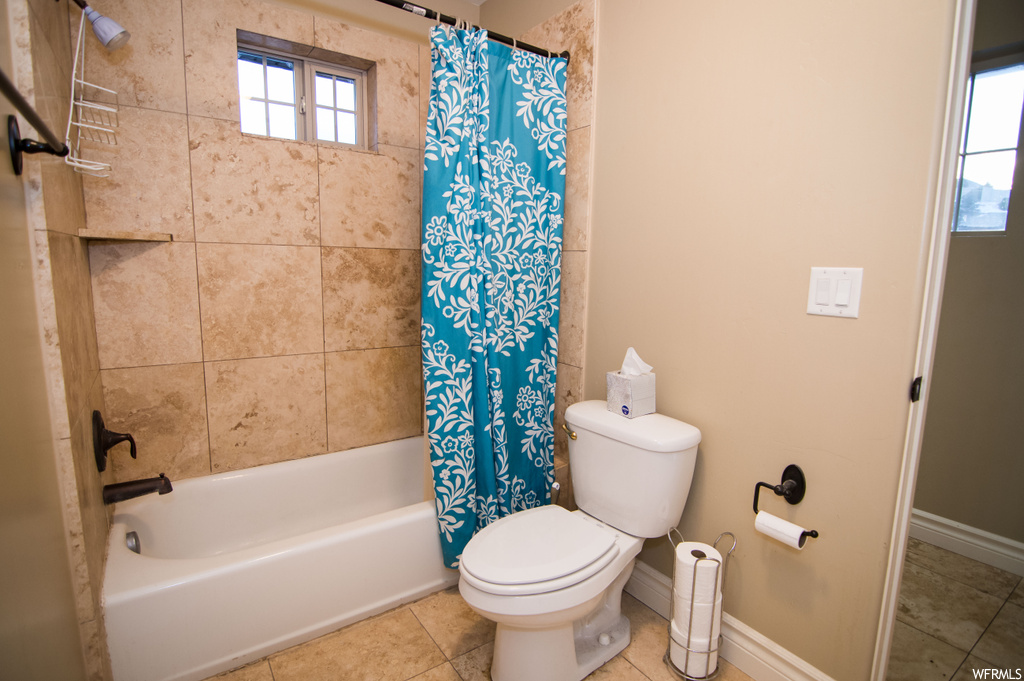 Bathroom with toilet, shower / tub combo with curtain, and tile flooring