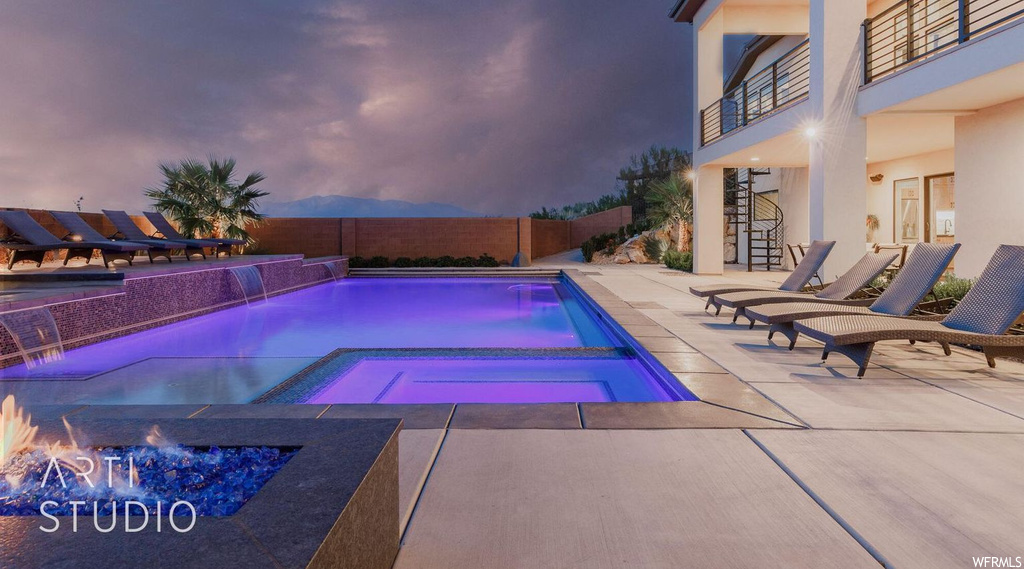 Pool at dusk with pool water feature, a patio area, an in ground hot tub, and a fire pit