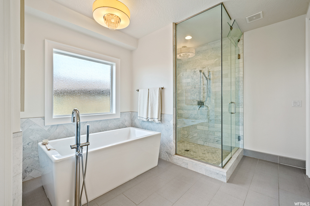 Bathroom with a textured ceiling, shower with separate bathtub, tile floors, and tile walls