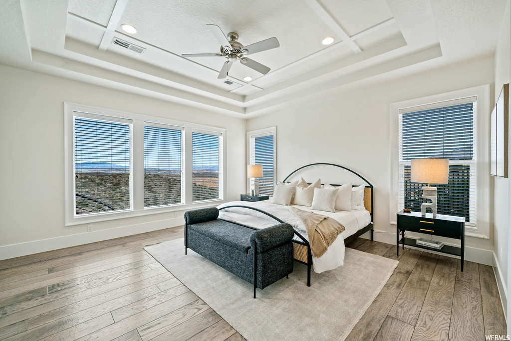 Bedroom featuring coffered ceiling, ceiling fan, light hardwood / wood-style floors, and a tray ceiling