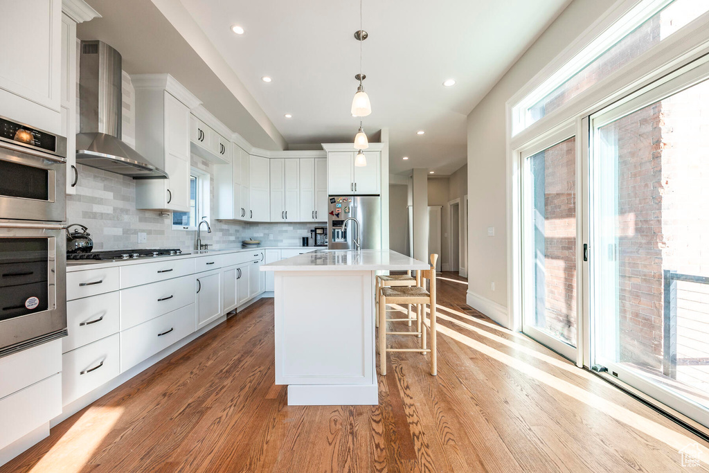 Kitchen featuring pendant lighting, a center island, tasteful backsplash, wall chimney range hood, and light hardwood / wood-style flooring