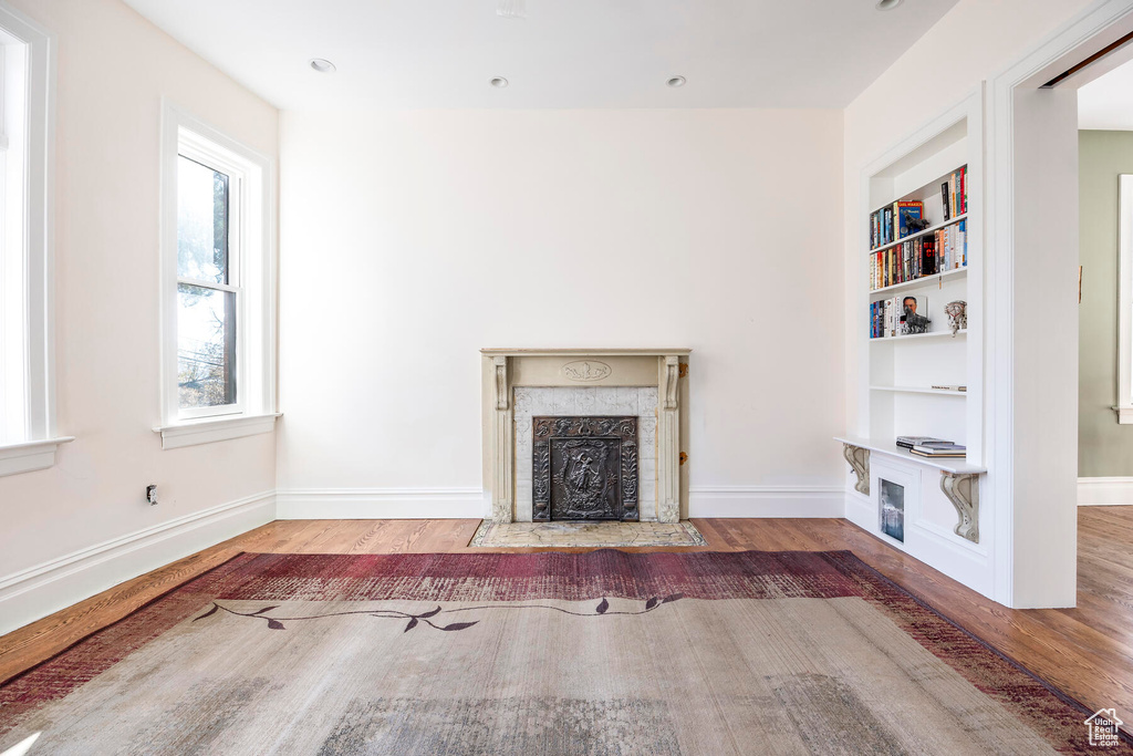 Unfurnished living room with a premium fireplace, built in features, and hardwood / wood-style floors